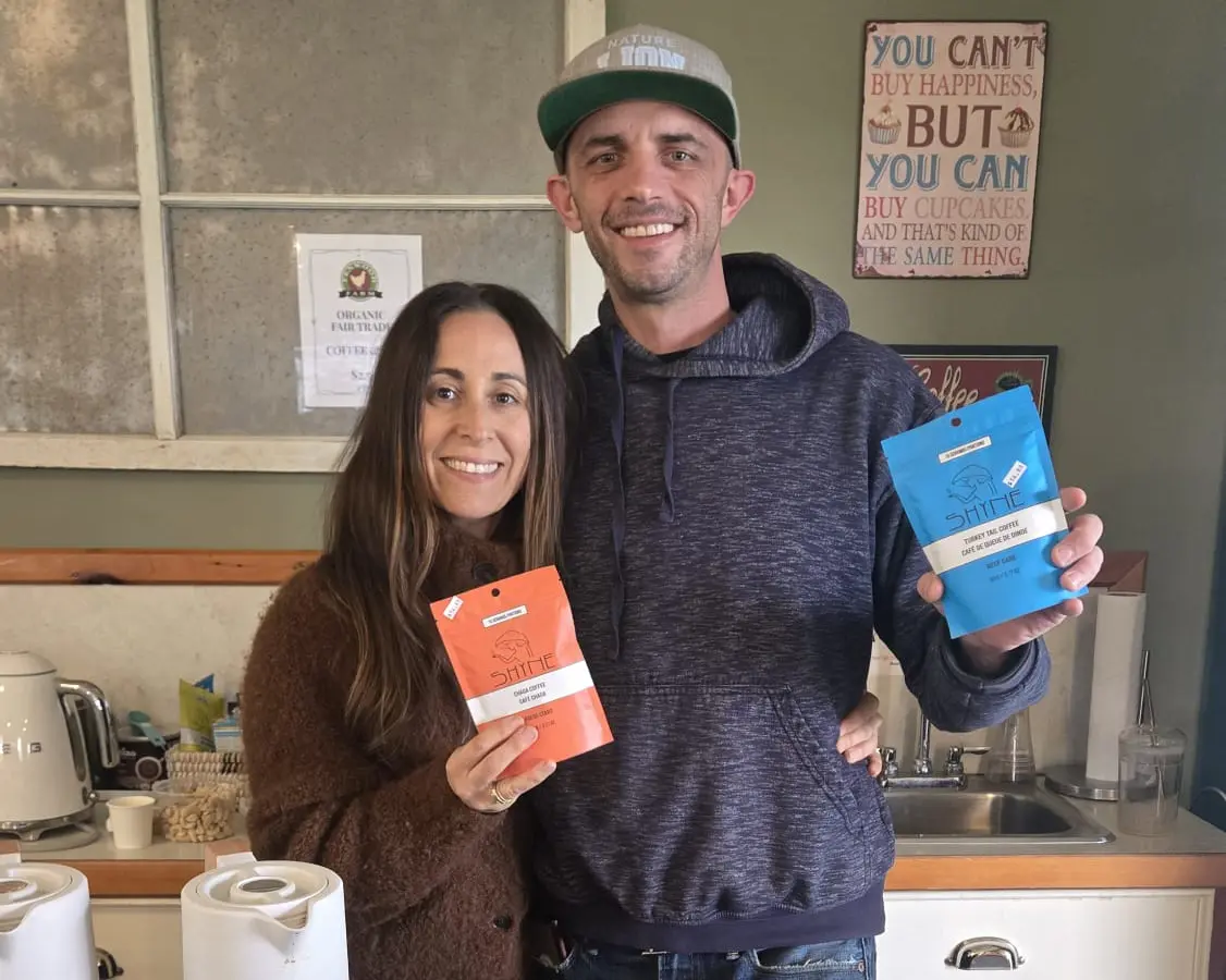 Nicole and Andrew, the founders of Shyne, behind a market table holding Chaga and Turkey Tail coffee pouches